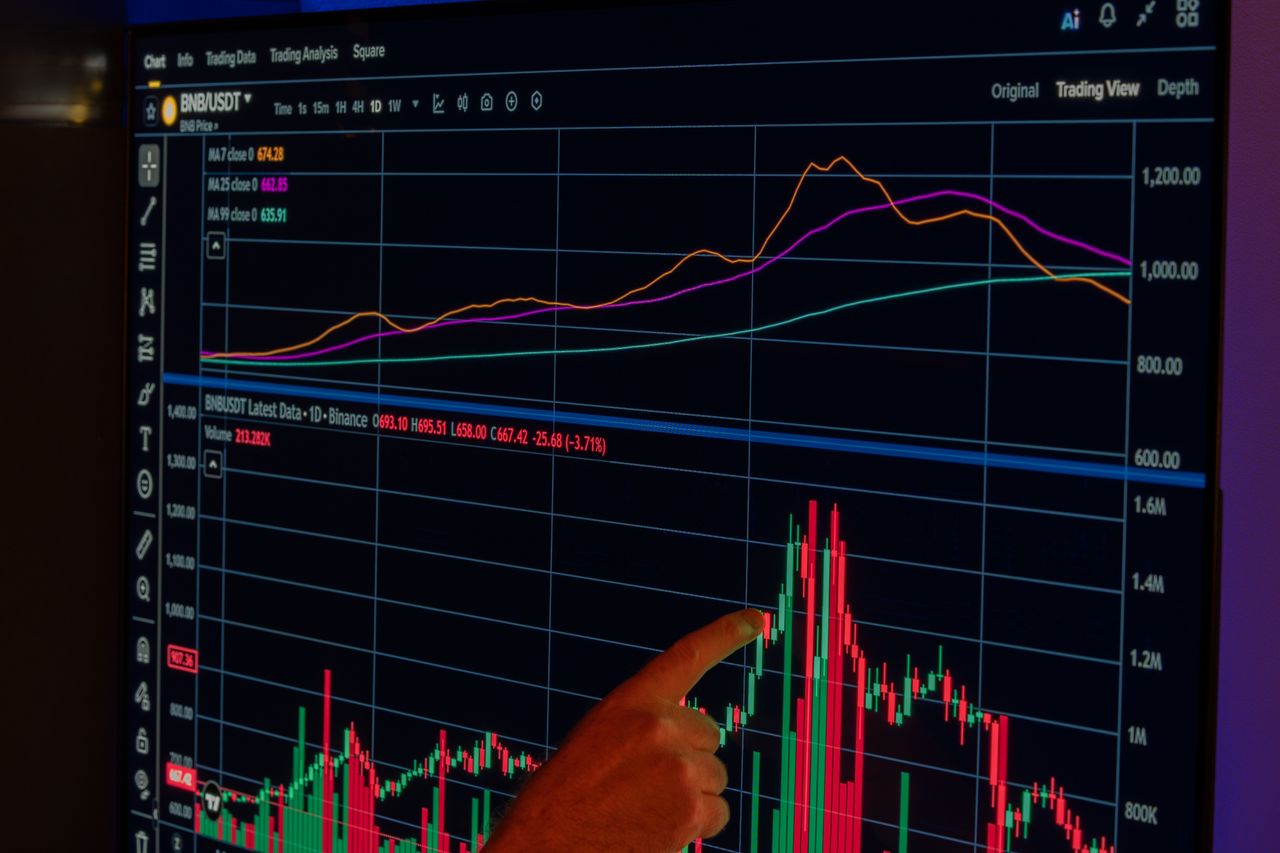 A hand points to a dynamic cryptocurrency market chart displayed on a screen, showcasing financial trends.